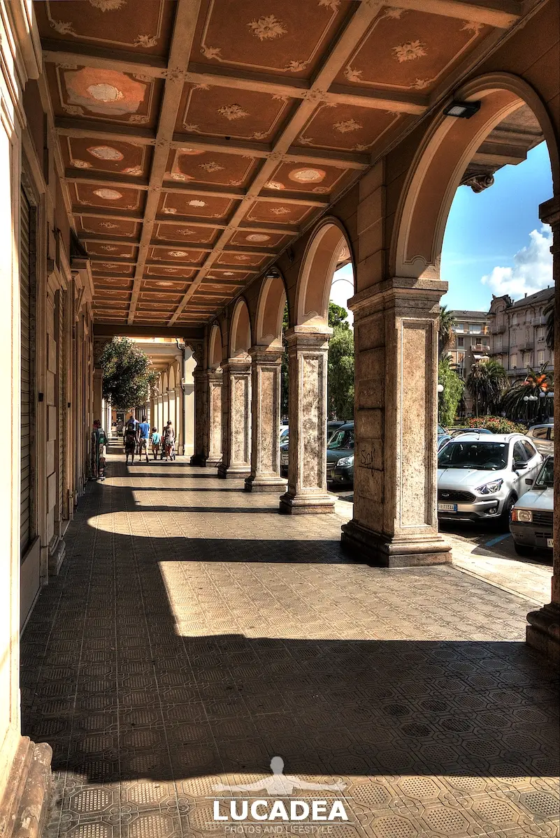 Portici di piazza Roma a Chiavari con arcate regolari e luce naturale che filtra tra colonne e ombre sul pavimento.