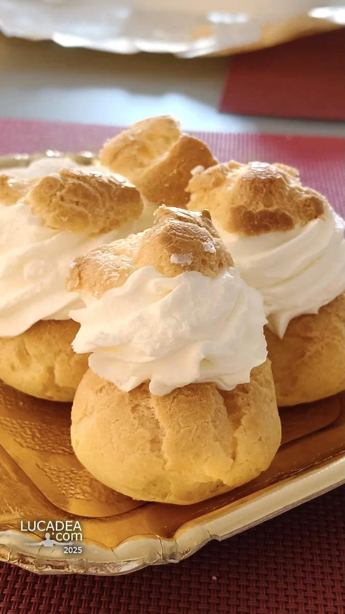 Cavolini con la panna su vassoio dorato, dolci liguri con crema soffice e pasta choux dorata, ripresi da vicino su tavolo.