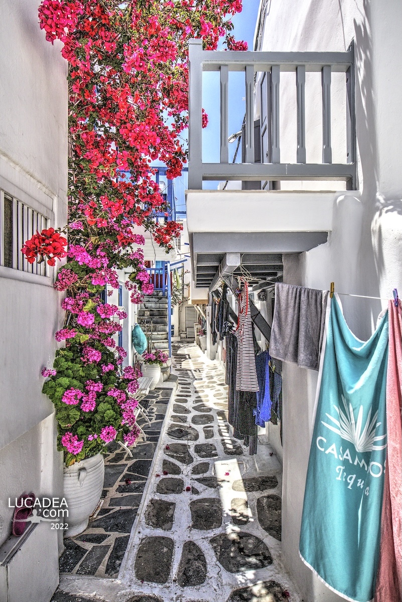 Scorci di Mykonos con bouganville rosa, terrazzi bianchi e asciugamani stesi tra pietre dipinte nell’isola