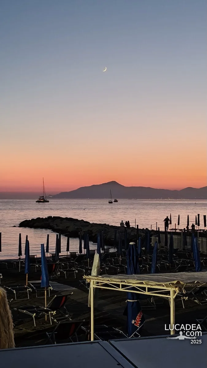 Tramonto alla Baia delle Favole a Sestri Levante con luna nel cielo, mare calmo e promontorio di Portofino sullo sfondo
