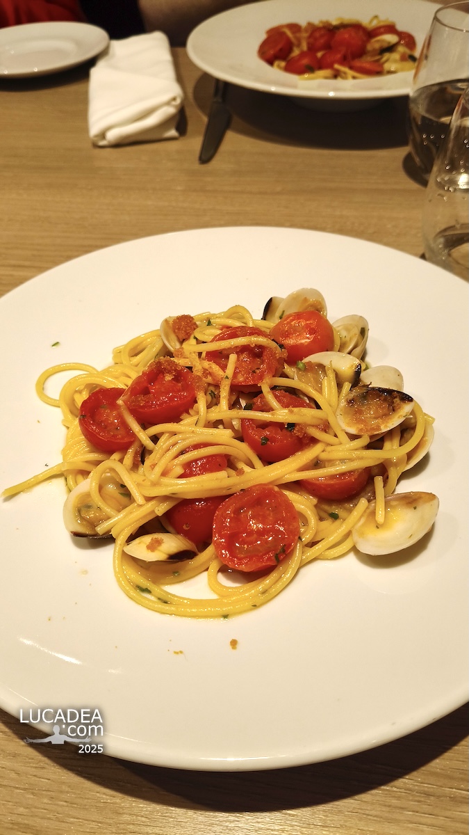 Piatto di spaghetti con vongole e pomodorini servito su tavolo in ristorante, con gusci aperti e pasta lucida ben condita