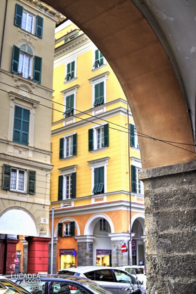 Portici del centro storico di Chiavari con palazzi gialli e persiane verdi incorniciati da un arco in primo piano