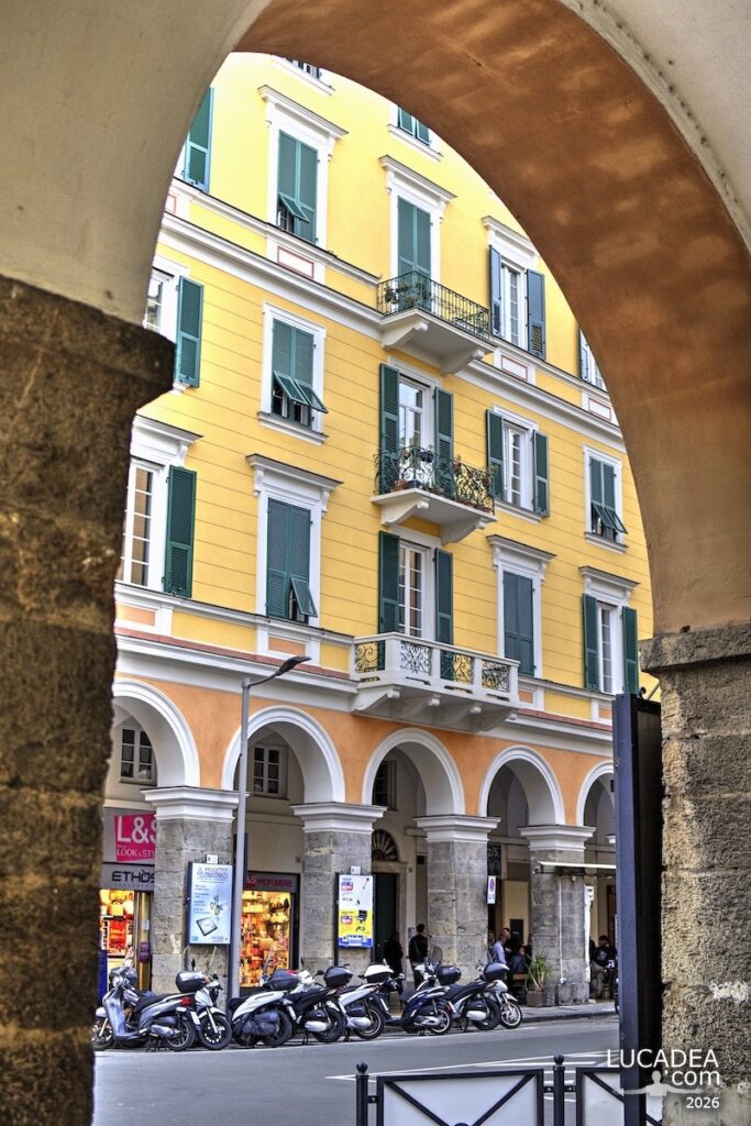 Portici del centro storico di Chiavari con palazzi gialli e persiane verdi incorniciati da un arco in primo piano