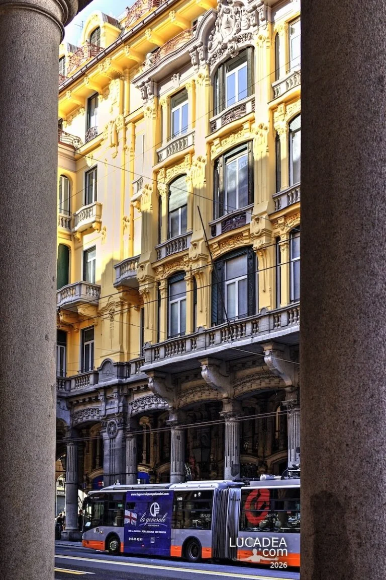 Portici di via XX Settembre a Genova con palazzo decorato giallo e autobus che passa tra le colonne