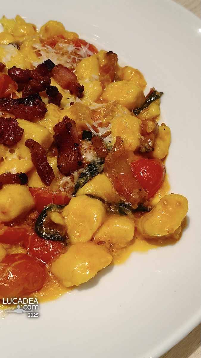 Gnocchi con pomodorini e guanciale serviti su piatto bianco con parmigiano e sugo cremoso in ambiente ristorante