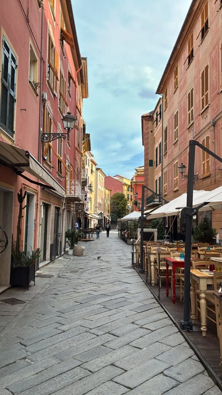 Il carruggio di Sestri Levante quasi vuoto al mattino, tra facciate colorate, pavimentazione in pietra e tavolini all'aperto